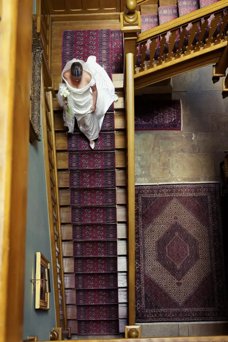 A bride seen from above on an oak staircase with a red runner