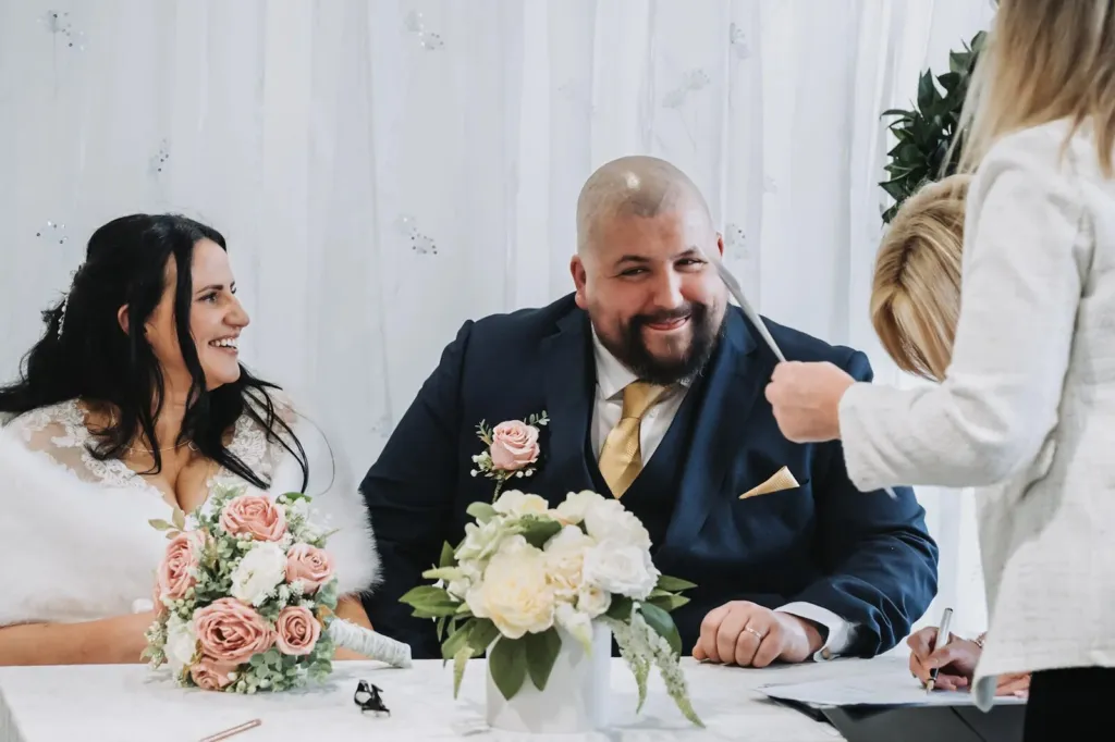 Bride and groom laughing at the register signing table with the registrar