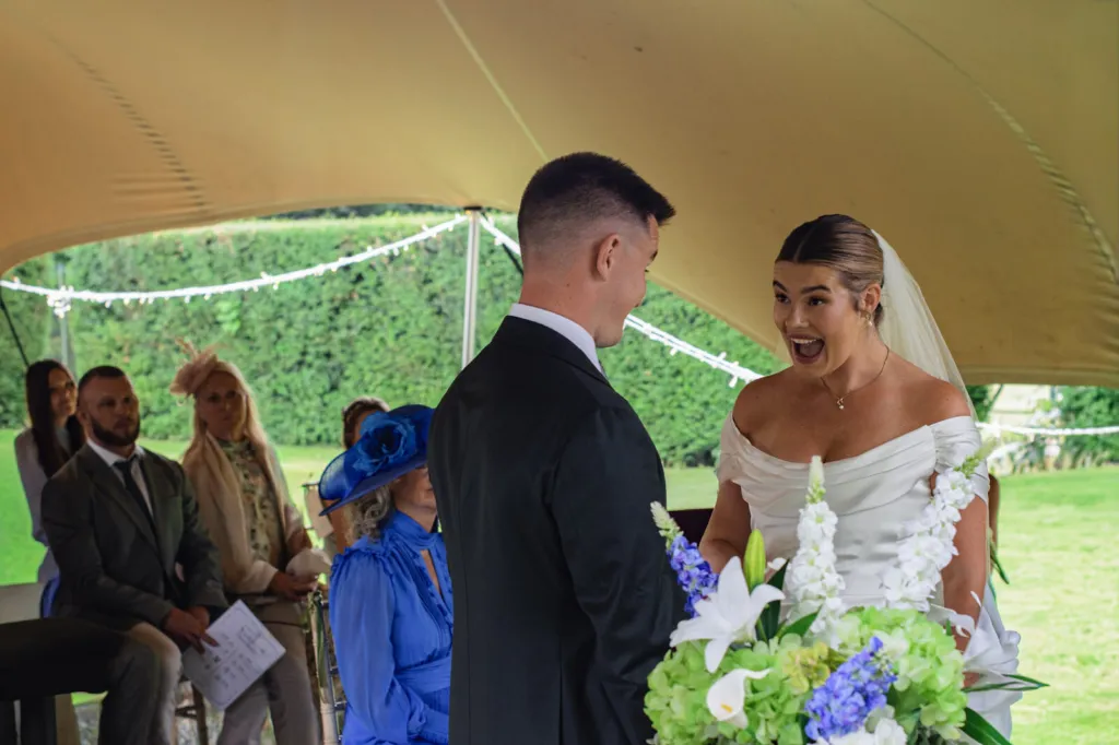 Lottie’s face as the vows begin under the stretch tent at Casterton Grange