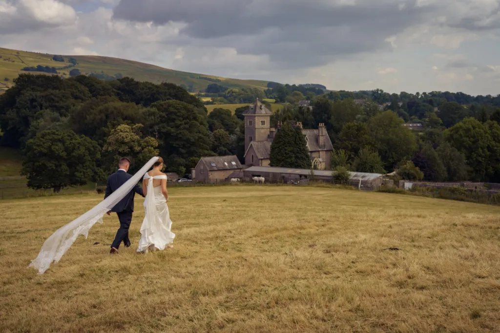 A couple walking across a meadow towards a stone tower under the fells