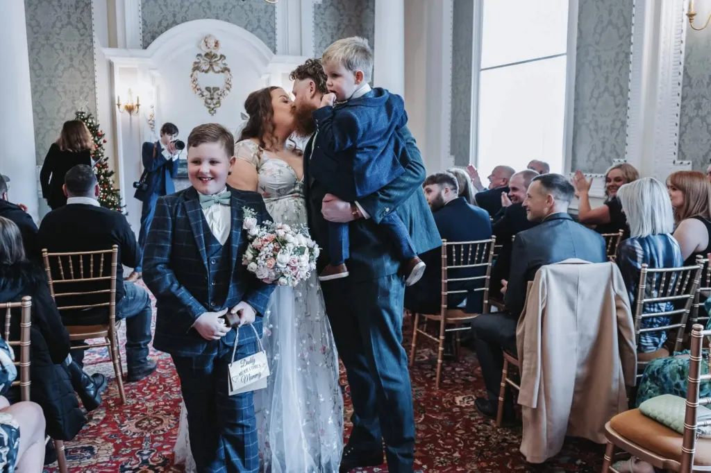 Groom carrying his son and kissing the bride as they leave the aisle
