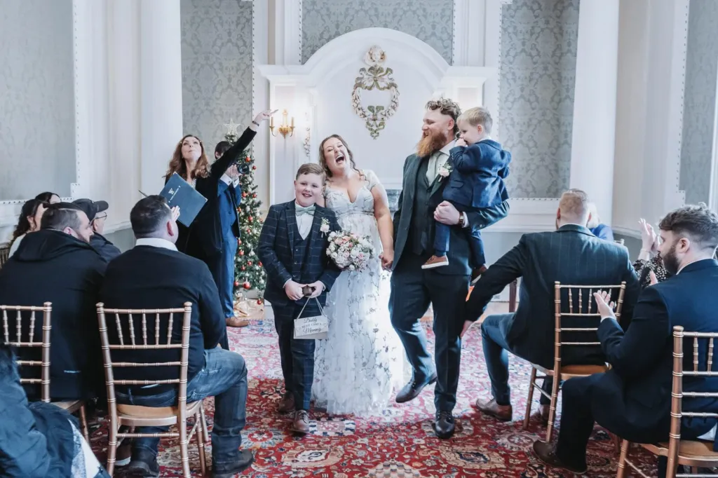 Newlyweds walking back down the aisle with their sons as guests cheer