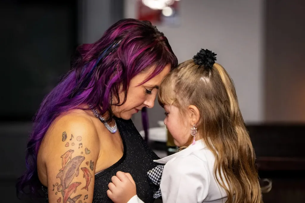 A mum with purple hair forehead to forehead with a young flower girl